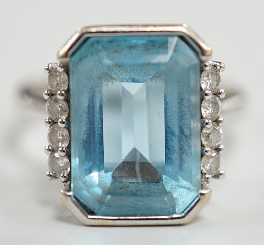 A 750 white metal and emerald cut blue topaz set dress ring, with diamond chip set borders, size O, gross weight 7.8 grams.